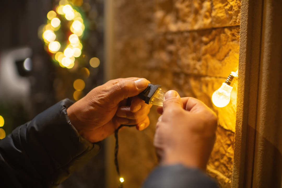 Deux mains branchant une prise, une ampoule éclairée en fond