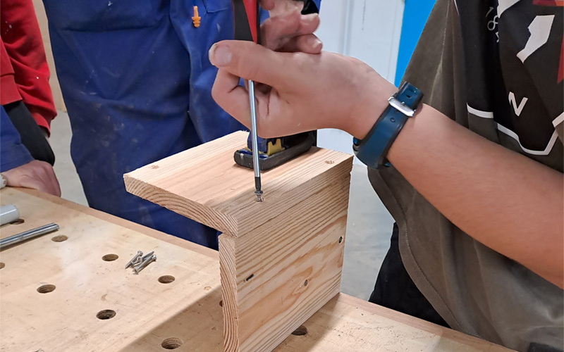 Une personne visse une vis pour assembler deux morceaux de bois et construire un nichoir