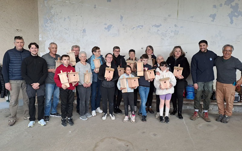 Un groupe de personnes avec des adultes et des enfants posent avec dans les mains les nichoirs en bois qu'ils ont contruits